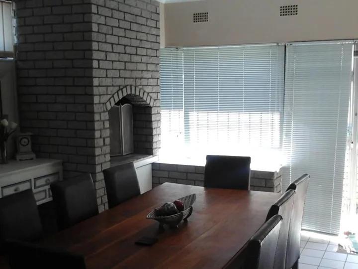 a dining room with a table and a brick wall at Shalom beach house in Bloubergstrand