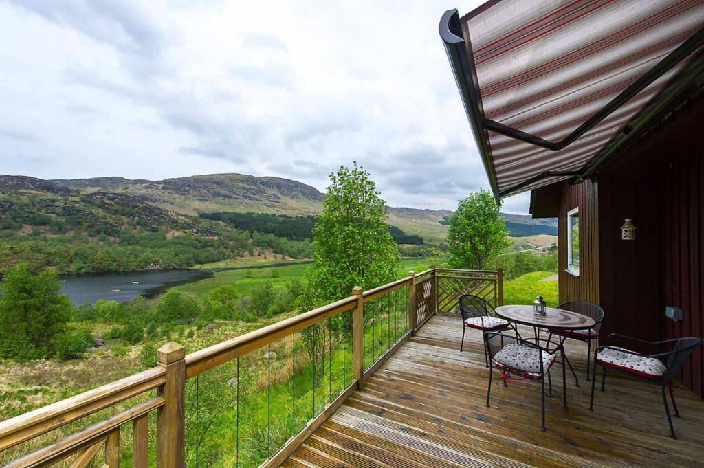 a balcony with a table and chairs and a view of a river at Kingfisher Lodge sleeps up to 4 in Crianlarich