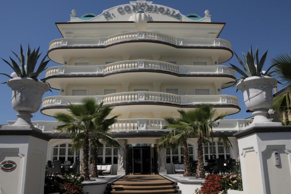 a large white building with palm trees in front of it at Hotel Conchiglia in Cervia