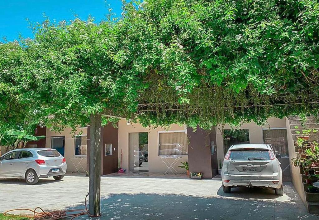 a tree with two cars parked in front of a building at Apartamento aluguel temporada Torres-RS in Torres