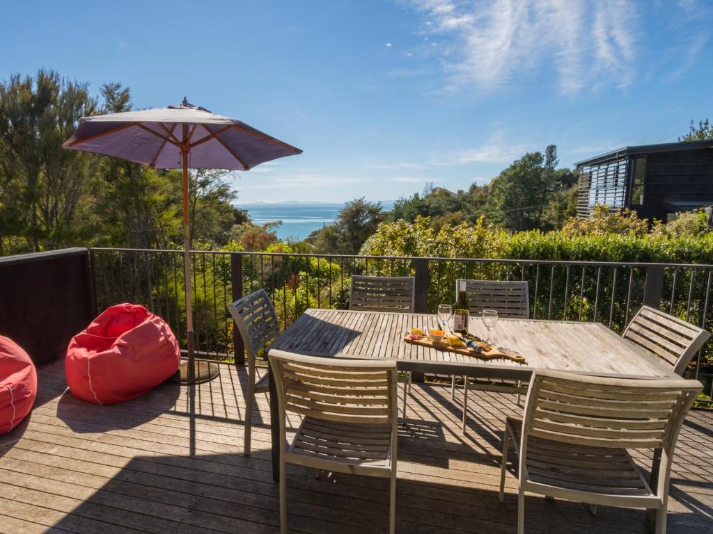 a wooden table with chairs and an umbrella on a deck at Bauhaus - Kaiteriteri Holiday Home in Kaiteriteri