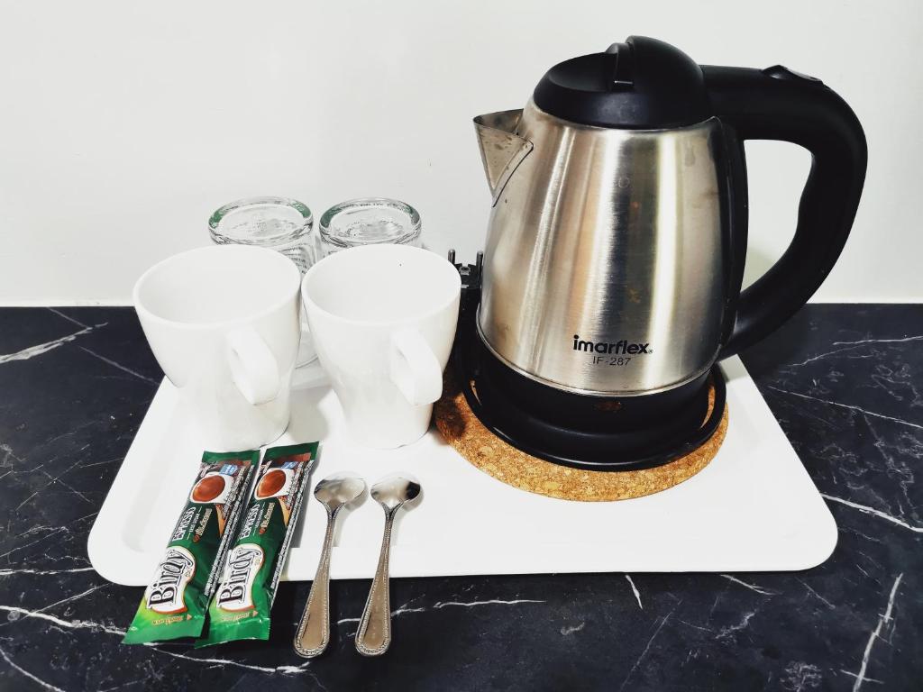 A tray with an electric kettle, cups, glasses, spoons and drink sachets.