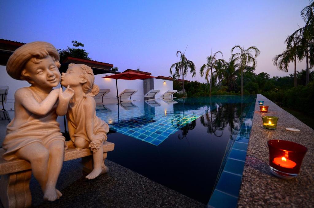 una estatua de dos niños sentados en un banco junto a una piscina en The Fusion Resort - SHA Extra Plus en Chalong 