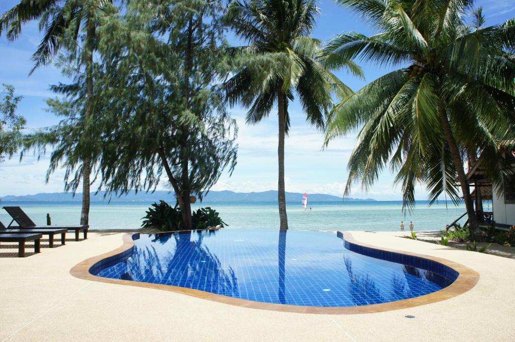 a swimming pool with palm trees and the ocean at Sarana Bungalows in Baan Tai