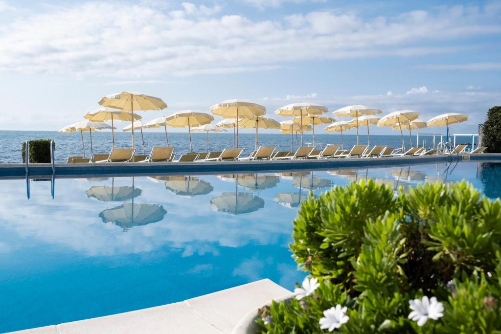 a swimming pool with chairs and umbrellas and the ocean at Hotel Cavalluccio Marino in Santa Marinella