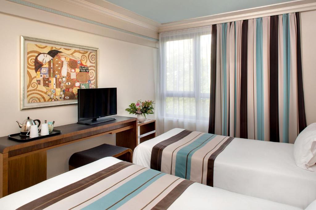 a hotel room with two beds and a desk with a television at Hotel Art Deco Euralille in Lille