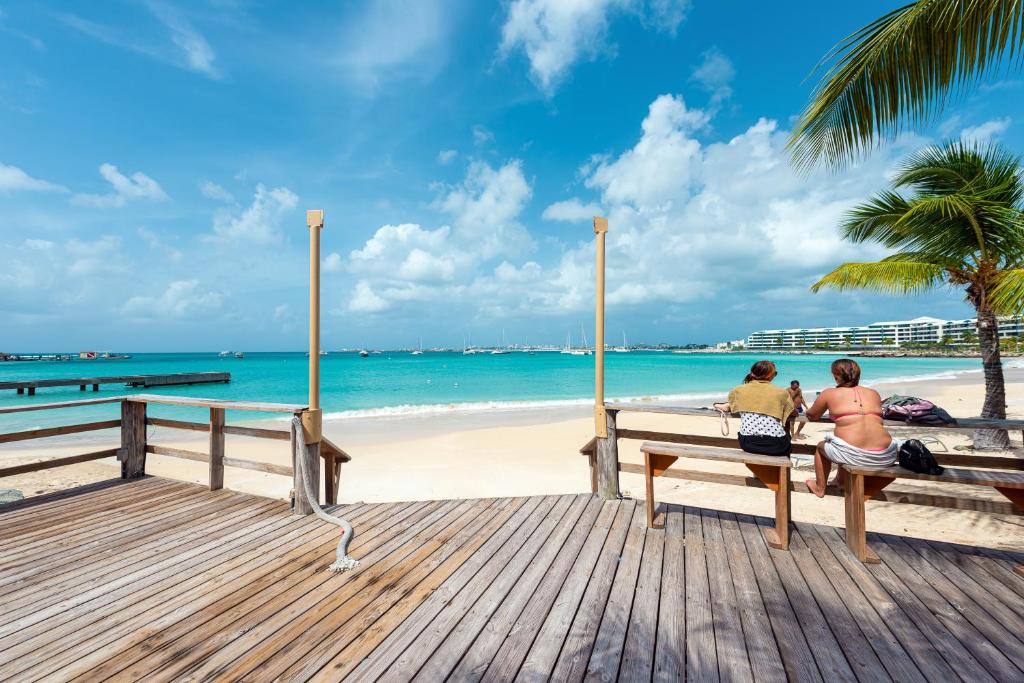 dos personas sentadas en un banco en la playa en Baker's Suites en Simpson Bay