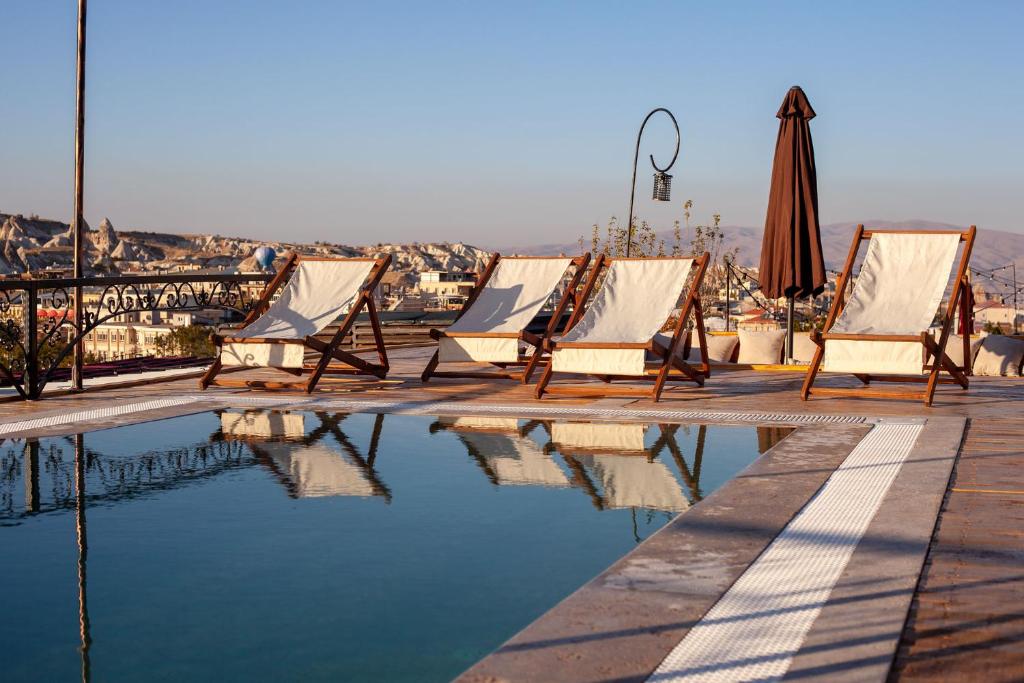 a row of lawn chairs and an umbrella next to a pool at Cappadocia Cave Rooms in Goreme