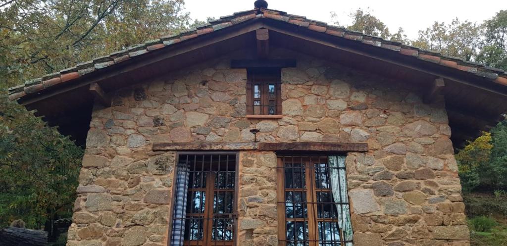 ein Steinhaus mit zwei Fenstern und einem Dach in der Unterkunft Cabaña Castañarejo in Candeleda