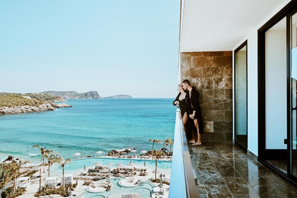 a bride and groom standing on a balcony overlooking the ocean at BLESS Hotel Ibiza - The Leading Hotels of The World in Es Cana