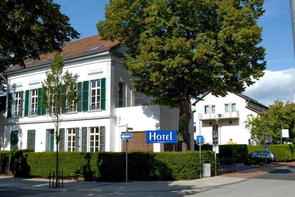 Hotel ZweiLinden Meckenheim Bonn في مكنهايم: مبنى أبيض مع علامة زرقاء أمامه