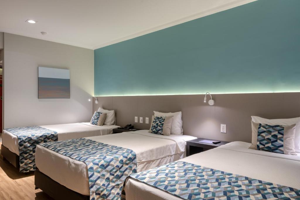 a room with three beds with blue and white sheets at Comfort Suítes Vitória in Vitória