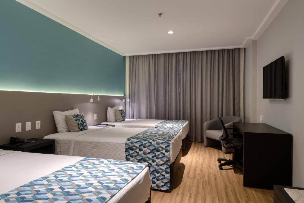 a hotel room with two beds and a desk at Comfort Suítes Vitória in Vitória