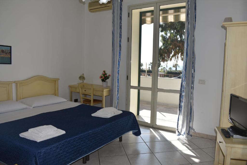 a bedroom with a bed and a television and a balcony at In Riva al Mare in Gela