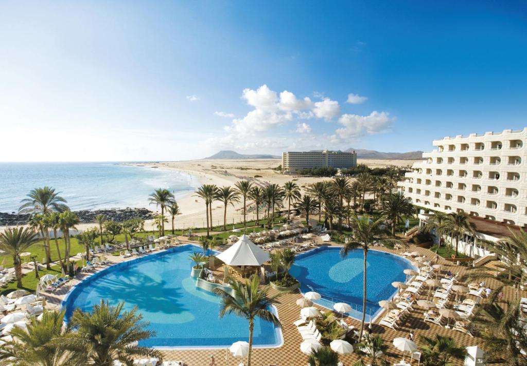 a beach with a pool, beach chairs, and a blue sky at Hotel Riu Palace Tres Islas in Corralejo