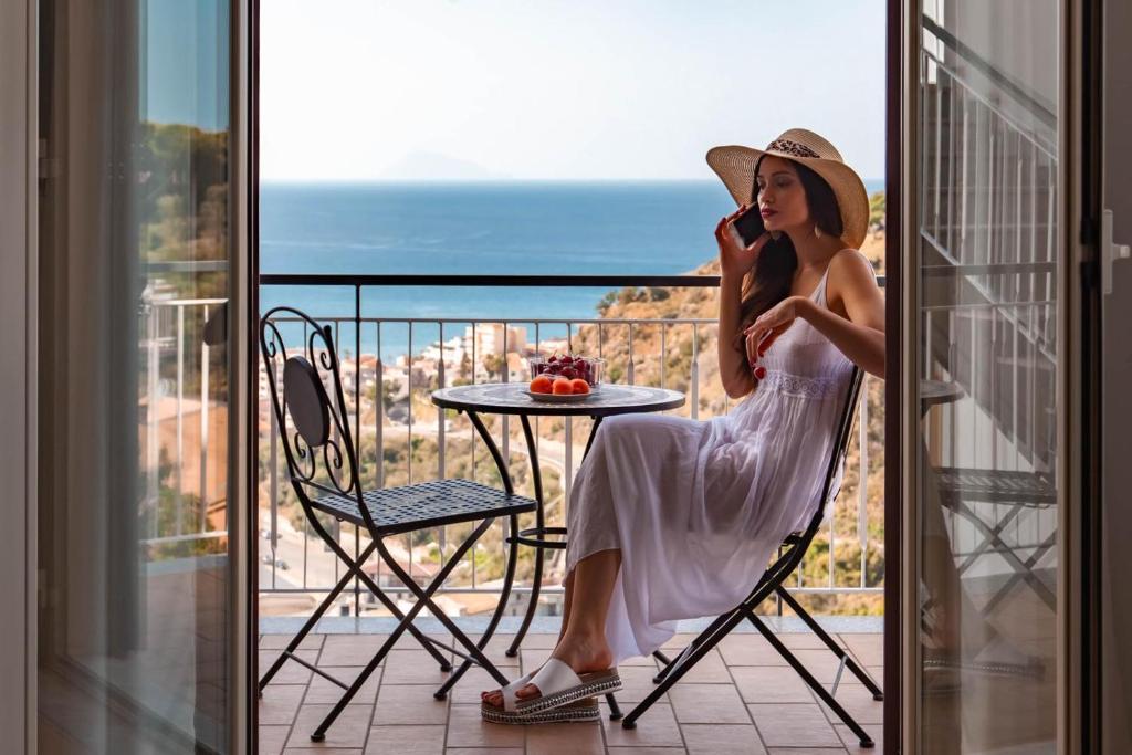 Eine Frau, die auf einem Balkon sitzt und auf einem Handy redet. in der Unterkunft San Martino Holiday Apartments in Capo dʼOrlando