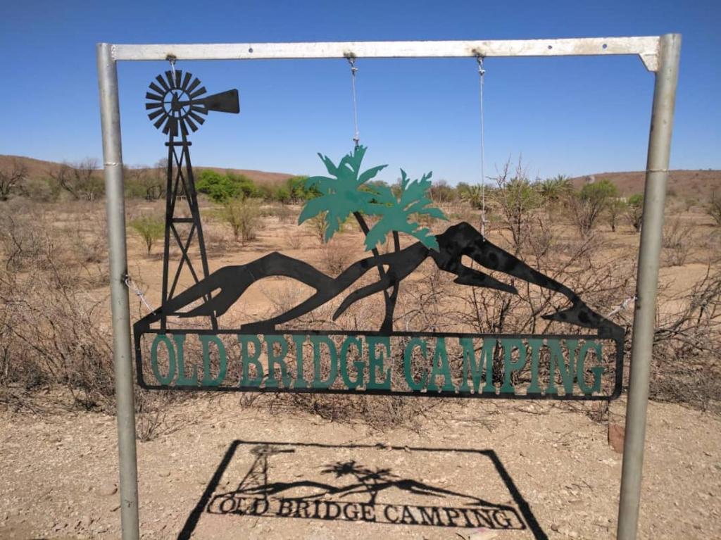 una señal en medio del desierto con un molino de viento en Old Bridge Camping en Maltahöhe