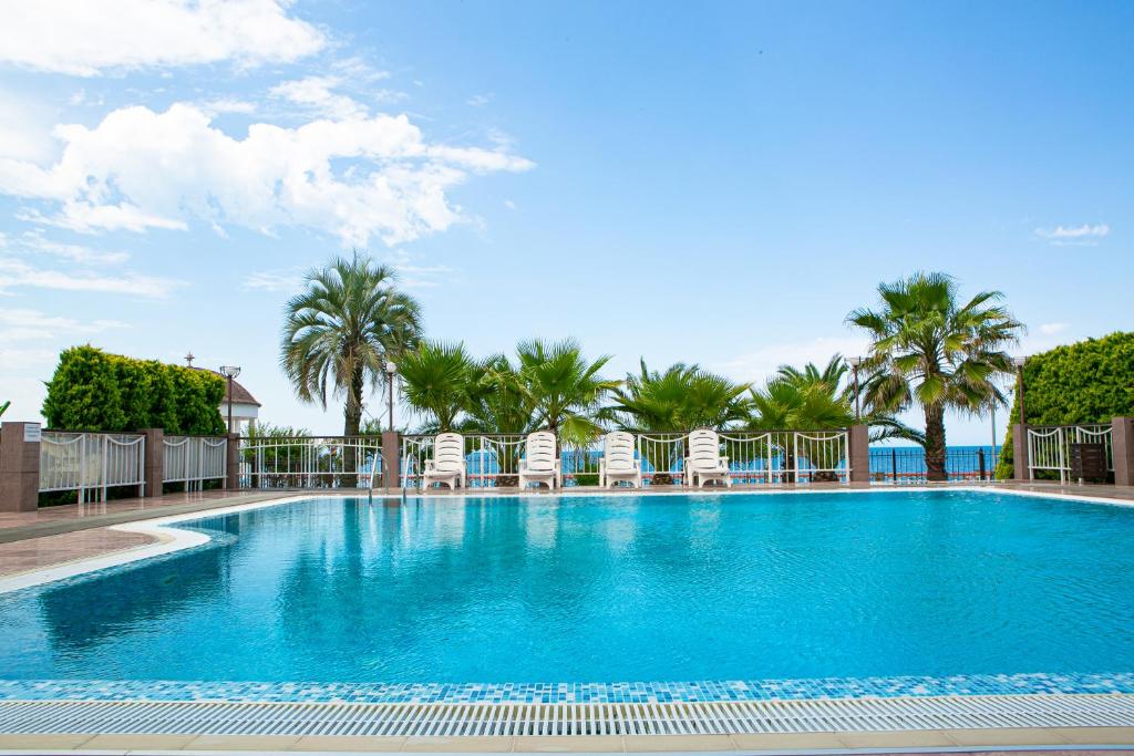 a large swimming pool with chairs and palm trees at Alex Resort & Spa Hotel in Gagra