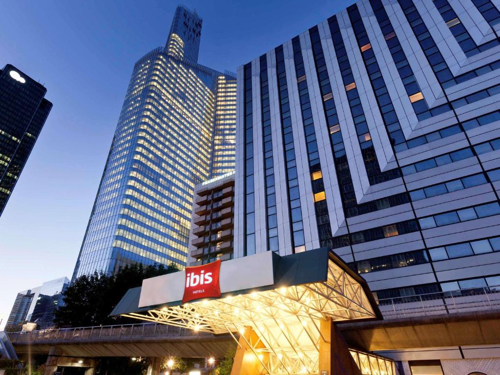 un grand bâtiment avec un panneau d'autobus devant lui dans l'établissement ibis Paris la Défense Esplanade, à Courbevoie