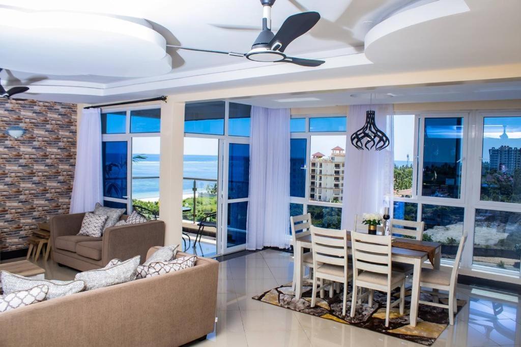 a living room with a table and chairs and windows at EMIRATES REEF APARTMENT 8D in Mombasa