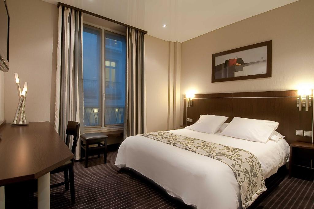 a hotel room with a bed and a desk and a window at Hotel Choiseul Opera in Paris