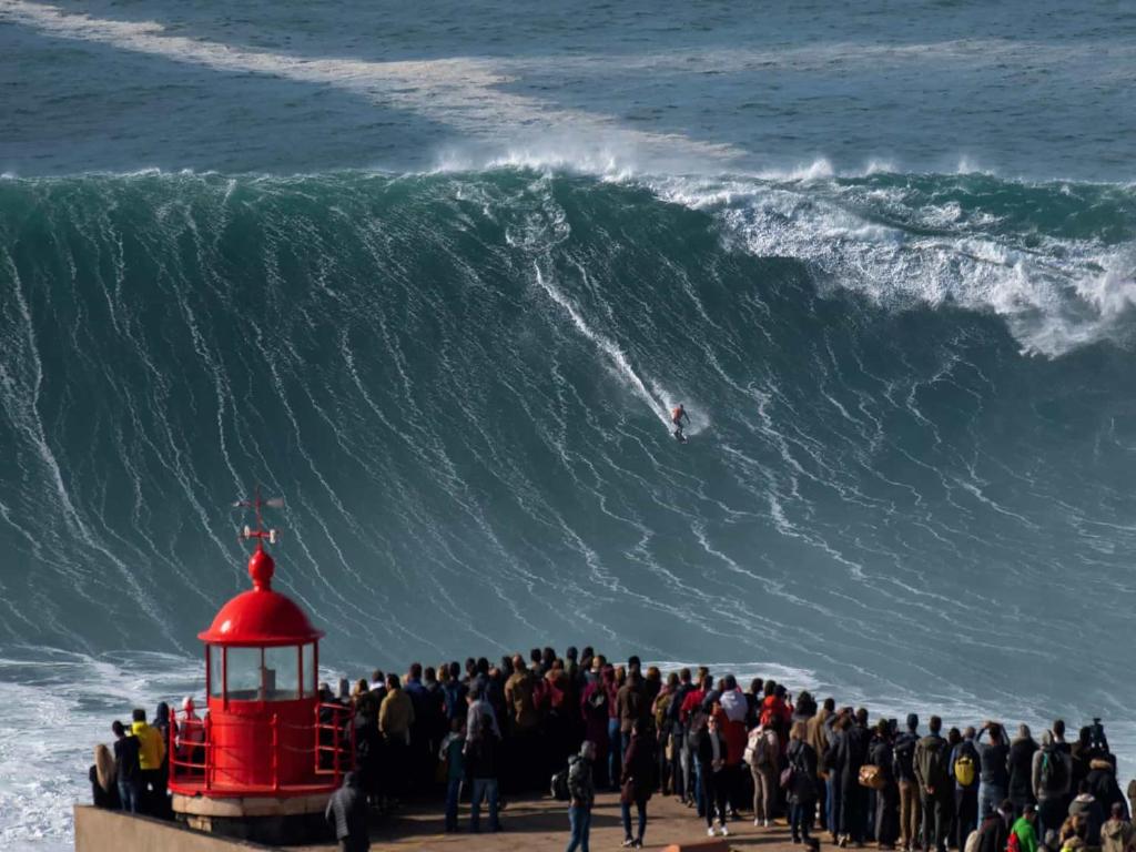 a group of people on a beach with a large wave at Hotel Mare in Nazaré