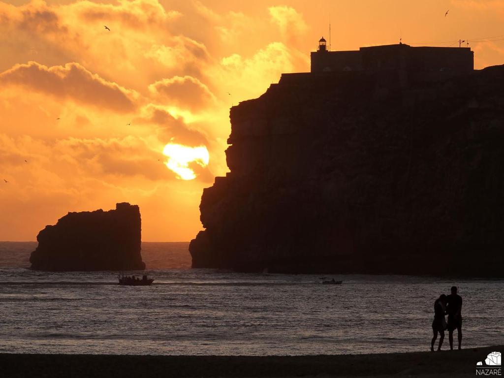a couple of people standing on the beach at sunset at Hotel Mare in Nazaré