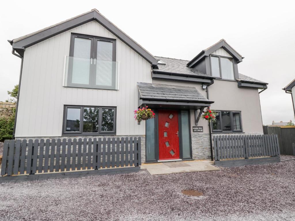 una casa bianca con una porta rossa e una recinzione di Meadow View a Benllech