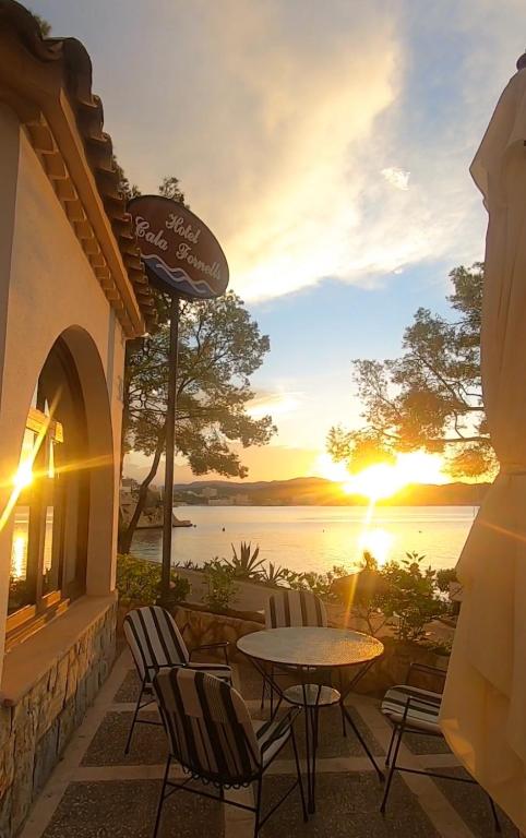 a patio with a table and chairs and a sunset at Hotel Cala Fornells in Paguera