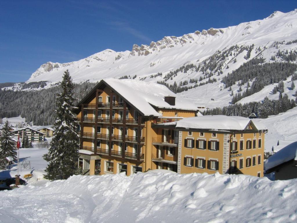 ein großes Gebäude im Schnee mit einem Berg in der Unterkunft Hotel Alpina Parpan in Parpan