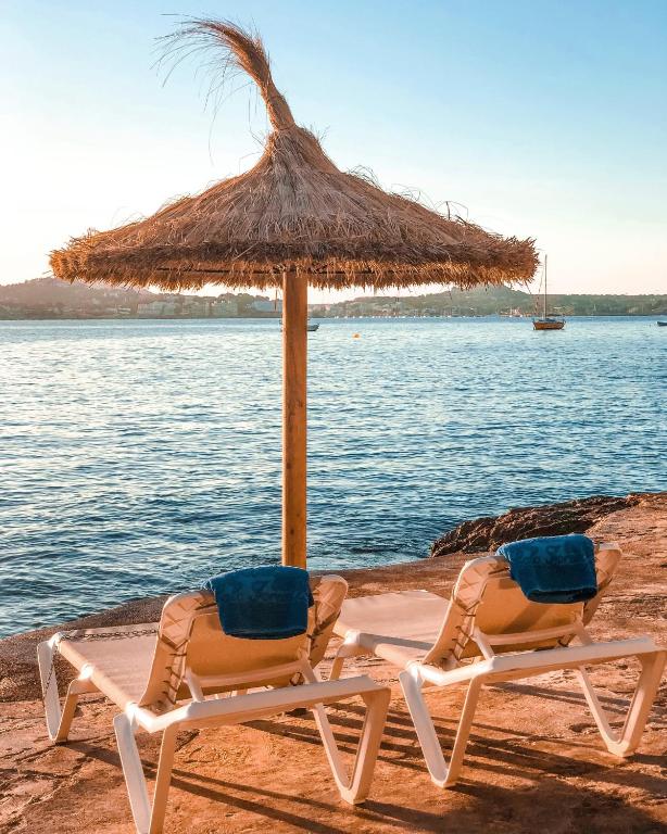 two chairs under a straw umbrella on a beach at Hotel Cala Fornells in Paguera