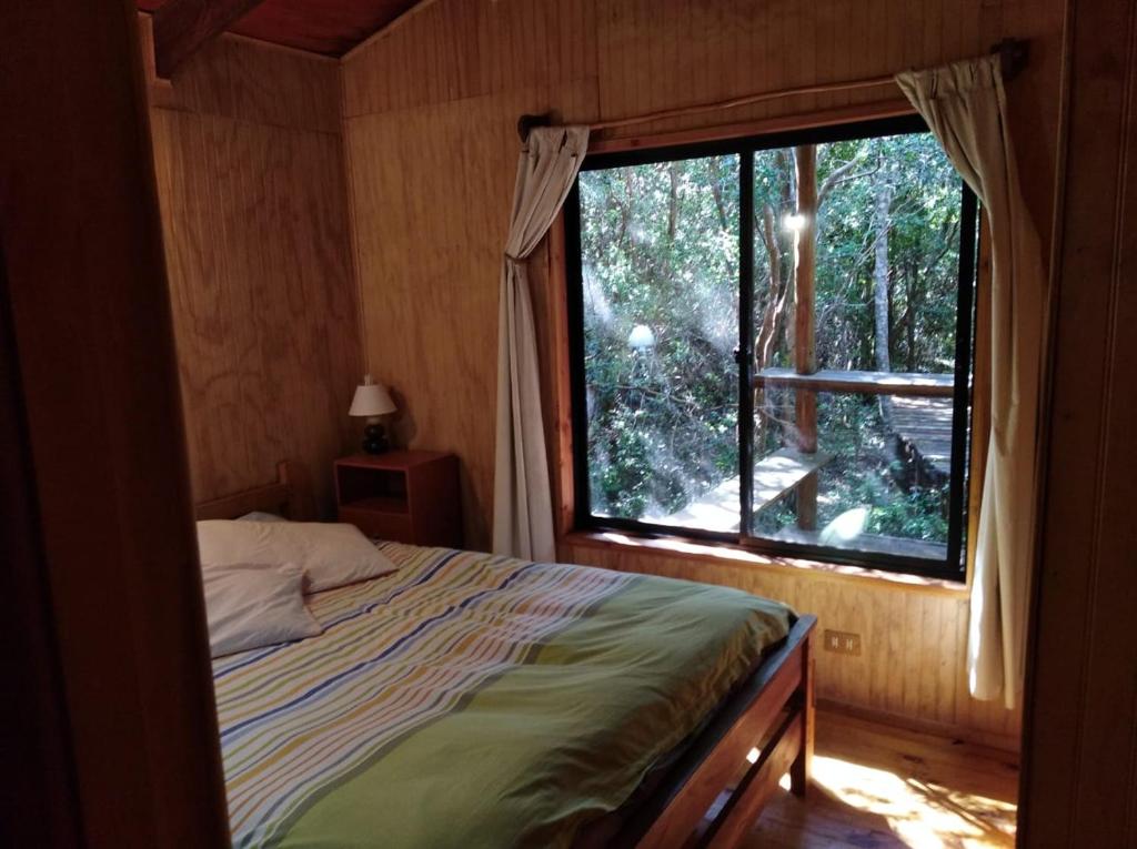 ein Schlafzimmer mit einem Bett und einem großen Fenster in der Unterkunft Cabaña en Río Puelo in Puelo