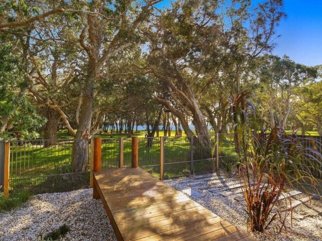 a wooden bench next to a fence with trees at The Wharf House at Budgewoi in Budgewoi
