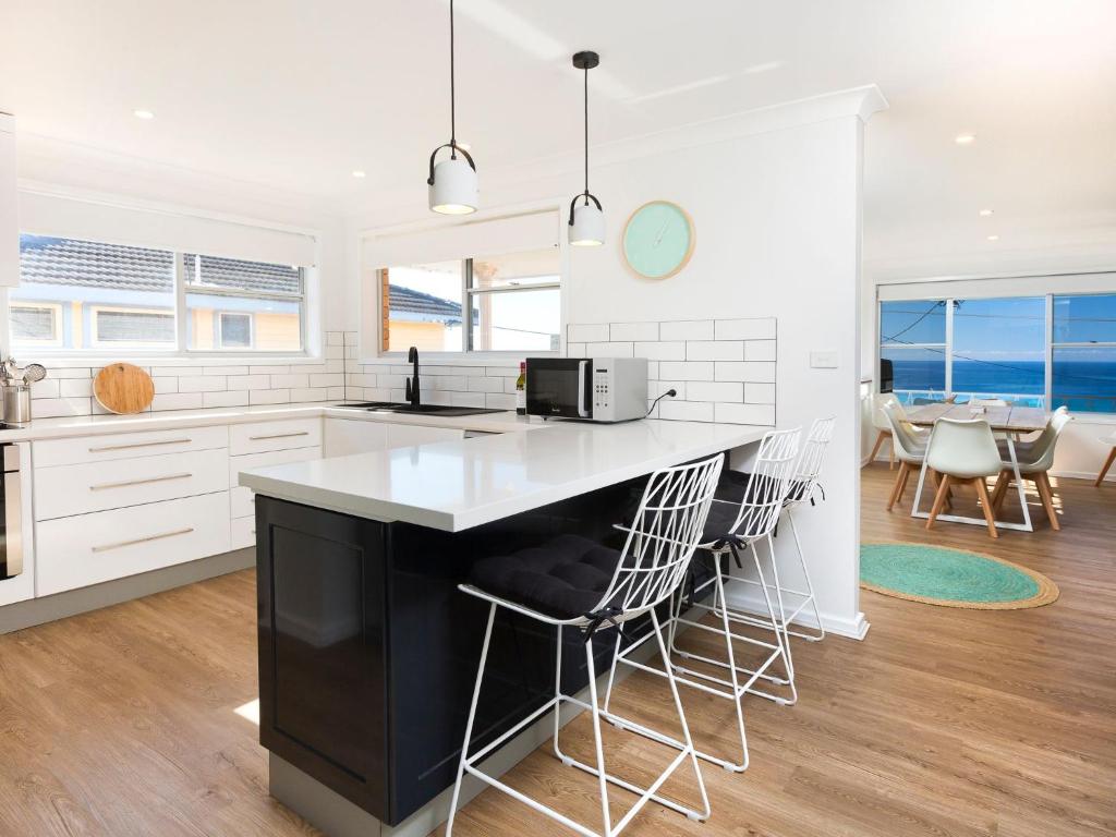 a kitchen with white cabinets and a black island with bar stools at Aqua Palm with Sweeping One Mile Views in Forster