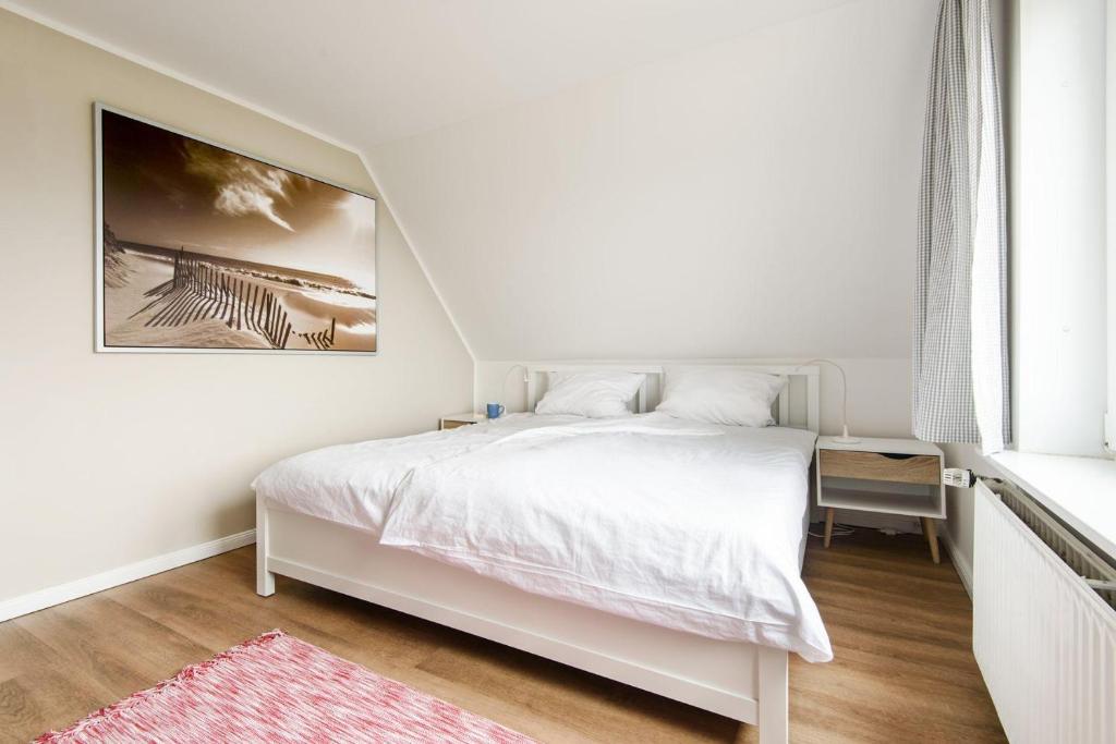 ein weißes Schlafzimmer mit einem Bett und einem Bild an der Wand in der Unterkunft LEE in Hörnum