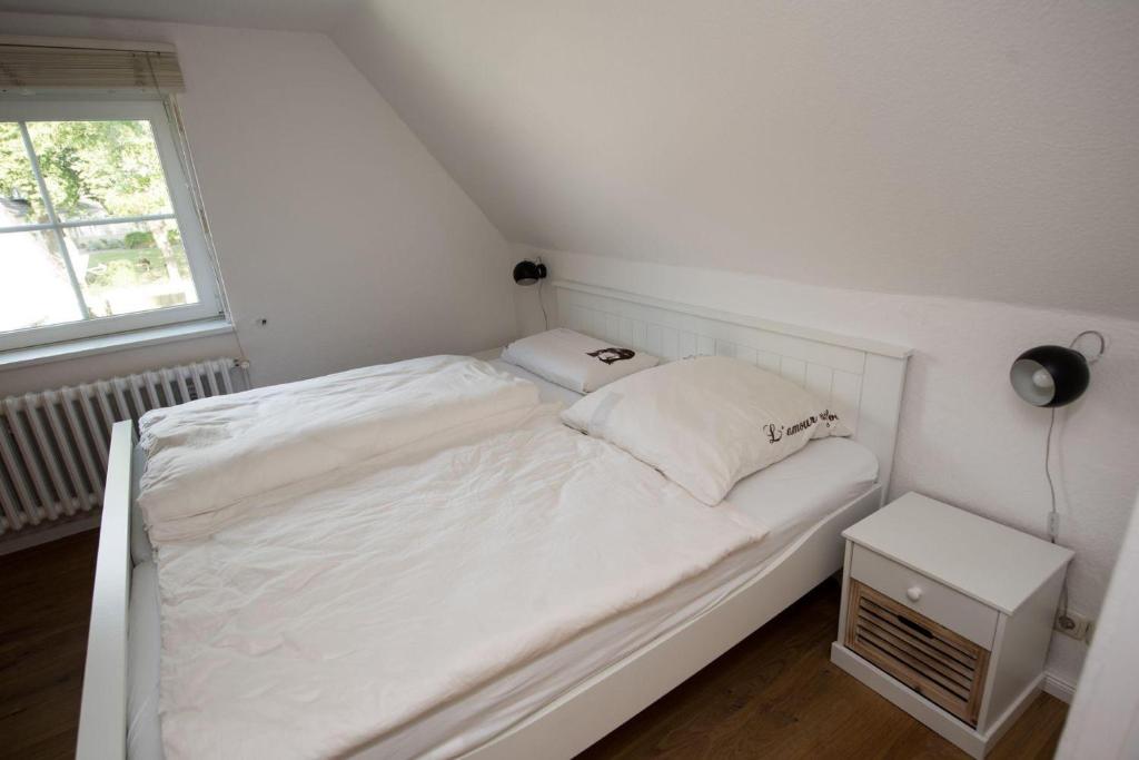 a small white bed in a room with a window at Schoenes-Ferienhaus-mit-Garten-Mid-Century-Moebeln-in-Strand-naehe-Avendorf in Avendorf auf Fehmarn