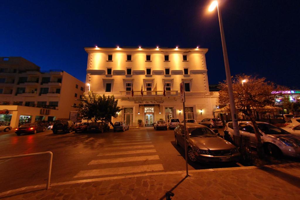 un edificio con coches estacionados en un estacionamiento por la noche en Hotel De La Ville, en Civitavecchia