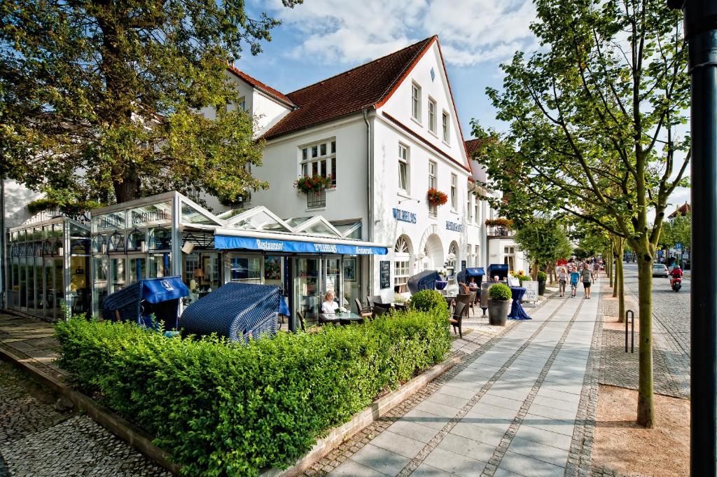a street with a white building and people sitting on a sidewalk at Neptun Hotel Kühlungsborn in Kühlungsborn