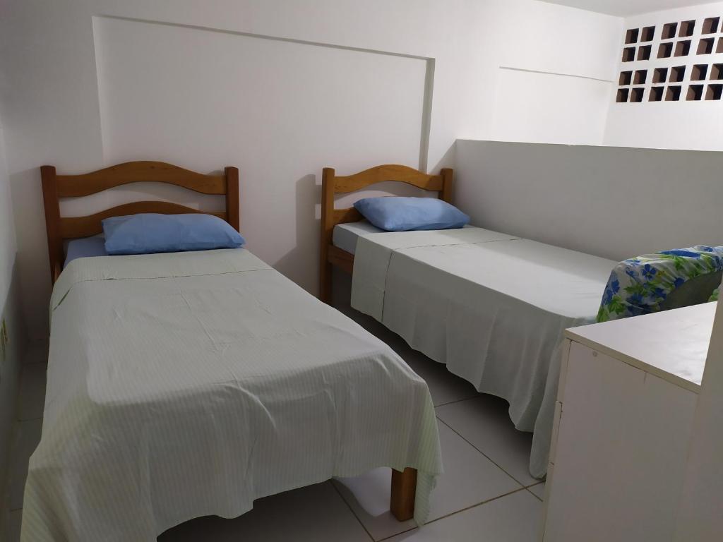 two beds in a room with white walls and blue pillows at Reserva dos Corais in Cabo de Santo Agostinho