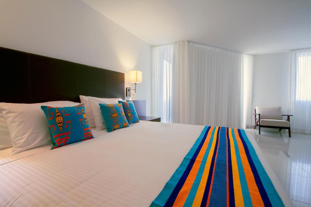 um quarto com uma grande cama branca com almofadas coloridas em Hotel Taroa em Ríohacha