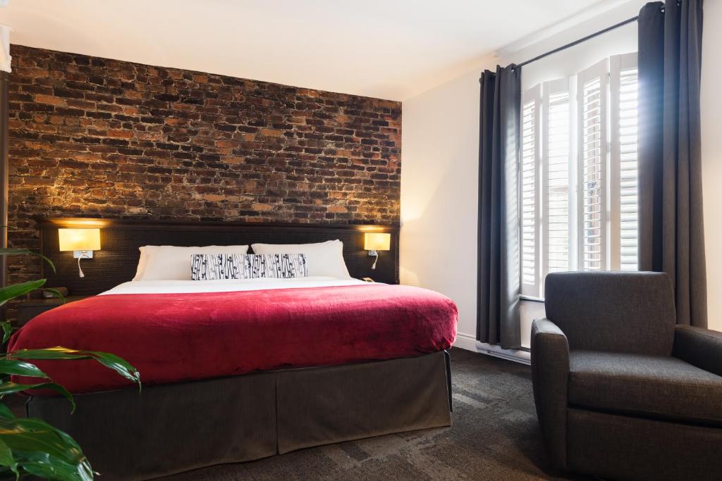 a bedroom with a brick wall and a bed and a chair at Hôtel des Coutellier in Quebec City