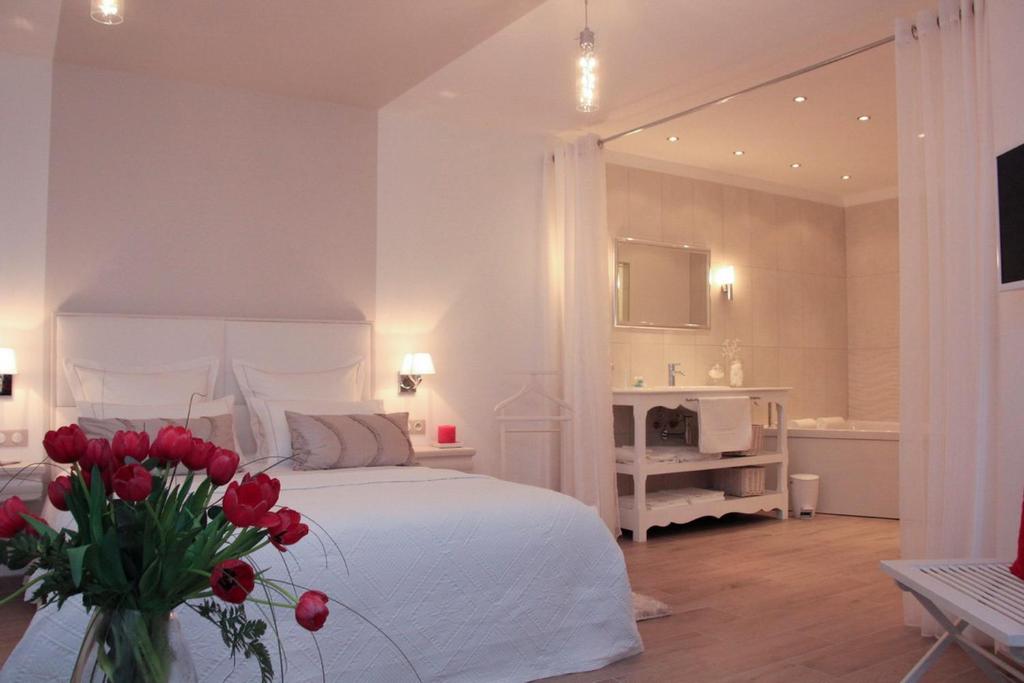 a white bedroom with a bed and a vase of red flowers at Au Coeur Des Hôtes in Steenvoorde