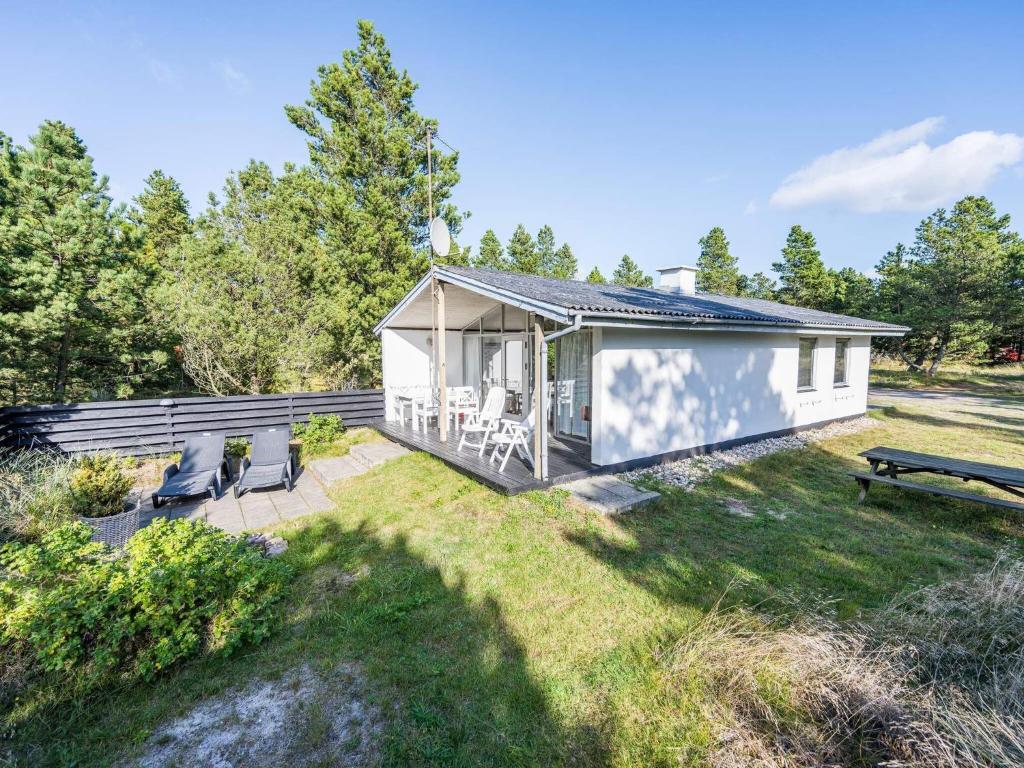 ein kleines weißes Cottage mit einer Terrasse und Stühlen in der Unterkunft Holiday home Blåvand CLI in Blåvand