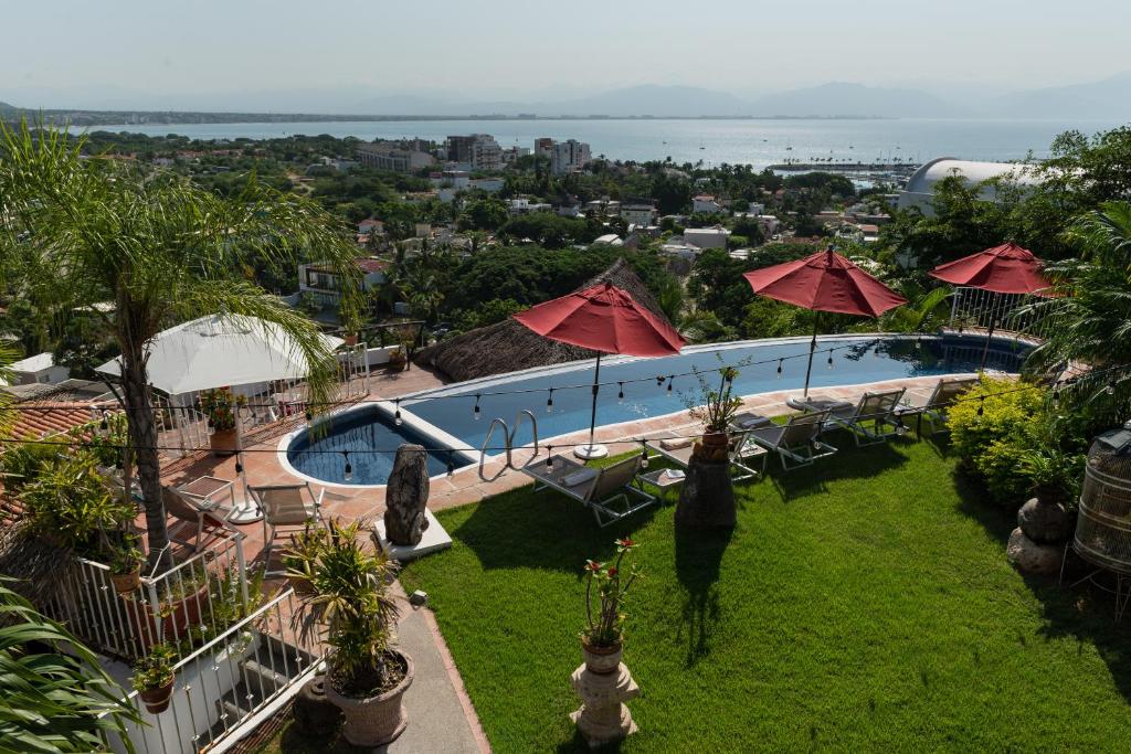 uma piscina com guarda-sóis e cadeiras vermelhas e o oceano em Villa Bella Bed & Breakfast Inn em Cruz de Huanacaxtle