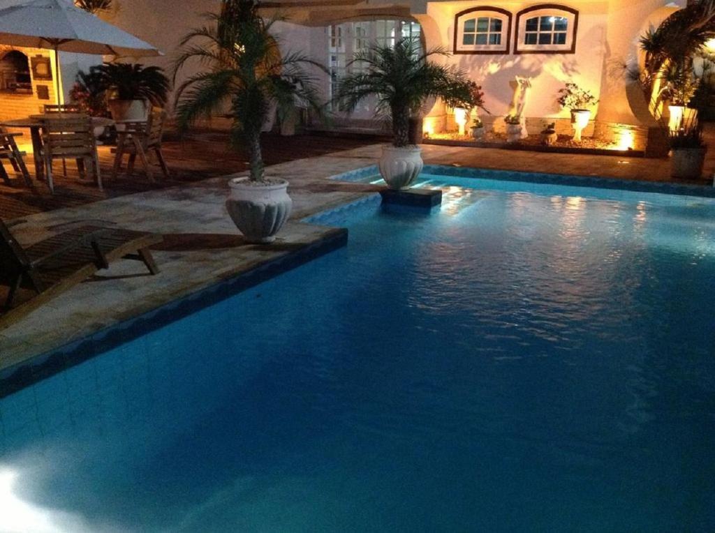 a large blue swimming pool with two potted palm trees at Perohouse in Cabo Frio