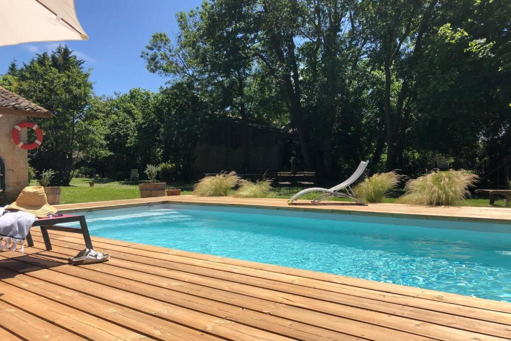 a swimming pool on a wooden deck with a bench and an umbrella at Gîte de Ker Val in Étauliers