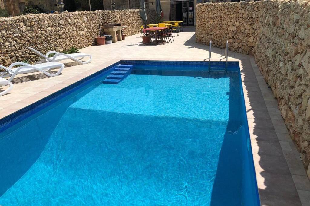 a large blue swimming pool next to a stone wall at Ta' Lorenzo Farmhouse in San Lawrenz