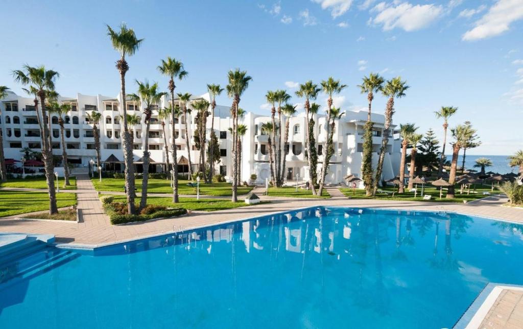 una piscina con palmeras frente a un edificio en L'Orient Palace Resort and Spa, en Sousse