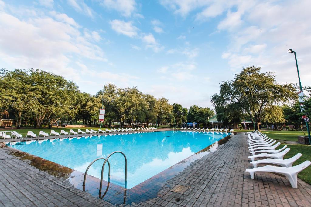 a large swimming pool with white chairs and trees at ATKV Eiland Spa in Letsitele