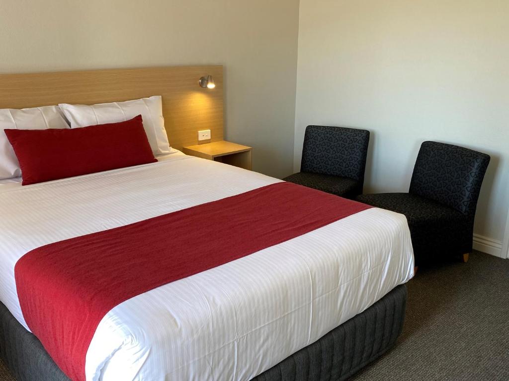 a hotel room with a large bed and two chairs at Country Gardens Motel in Coonabarabran